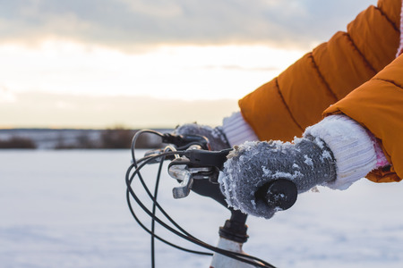 the girl put her hands on the wheel of a bicycle against the background of the winter riverの写真素材