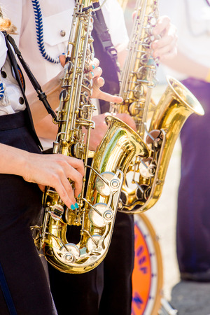 Girls play saxophones on  clear sunny day on  street. Festive concert in  city. Two saxophones in  hands of girlsの写真素材