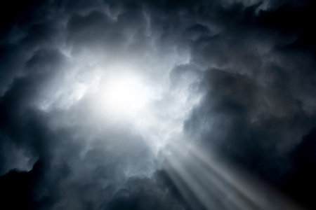 The ray of sunshine breaks through dark stormy clouds. Symbol of the struggle of good and evil.の写真素材