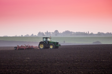 In the field a tractor works in the morning during the sunriseの写真素材