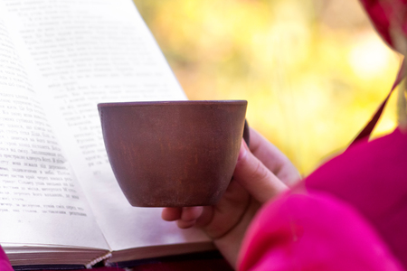 A girl with a cup of coffee reads a book in the natureの写真素材