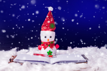 Toy snowman in front of an open book. Fiction reading. Snowman on a dark background during the snowfall. Happy Christmas and New Year's greetingsの写真素材