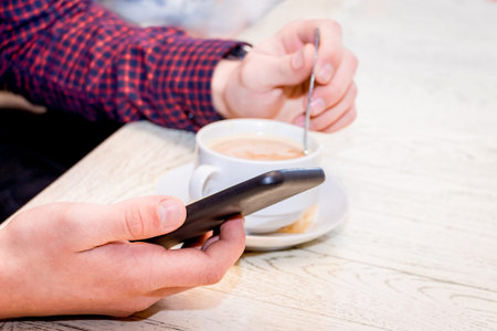 A young man in a cafe drinks coffee and has fun with the help of a mobile phone