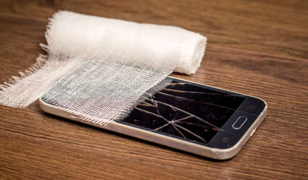 Bandage near the damaged phone. The damaged smartphone needs to be repairedの写真素材