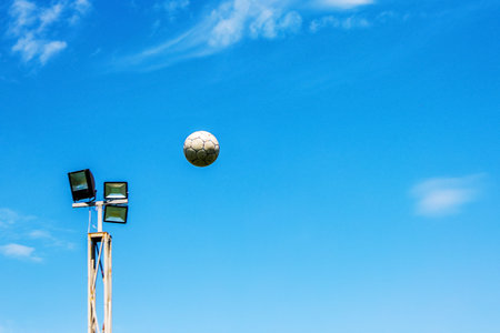 The soccer ball is high in the sky at the lamp