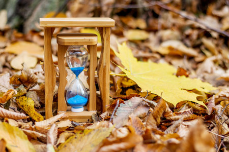 Sands clock and yellow maple leaf on the background of dry autumn leaves