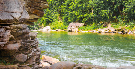 Rock made of many layers of stones near a mountain river in summer