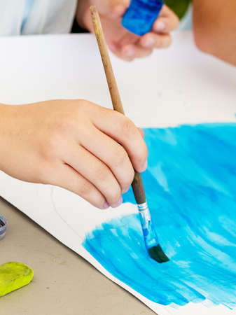 Girl performs drawing on paper blue paint. Girl holds a brush in her hand while drawingの写真素材