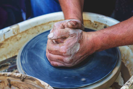 The potter forms a future product from a piece of clay on a potter's wheel. Potter's hands at workの写真素材