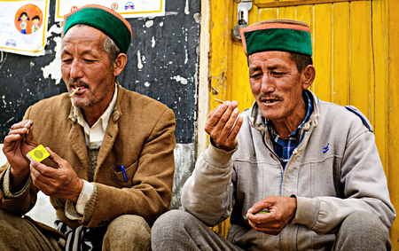 Sangla, India- May 01, 2016: Indian men of Himachal Pradesh state of India in traditional Kinnaur hats in Himalayas lighting cigarettsのeditorial素材