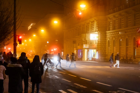 A captivating photograph captures the essence of a Christmas photowalk in Salzburg, Austria. The scene is shrouded in a mystical, foggy atmosphere, with warm, golden light emanating from street lamps and Christmas decorations. Pedestrians cross a street, their figures silhouetted against the glow, while a car's headlights cut through the fog. The architecture of Salzburg's buildings provides a beautiful backdrop, creating a magical and festive ambiance.の写真素材