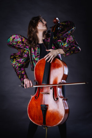 A captivating portrait of a cellist against a dark background. She is elegantly dressed in a floral patterned jacket and black pants, holding a cello and bow with grace and focus. The lighting highlights her features and the rich tones of the instrument, creating a dramatic and artistic composition. Perfect for representing music, art, culture, and talent.の写真素材