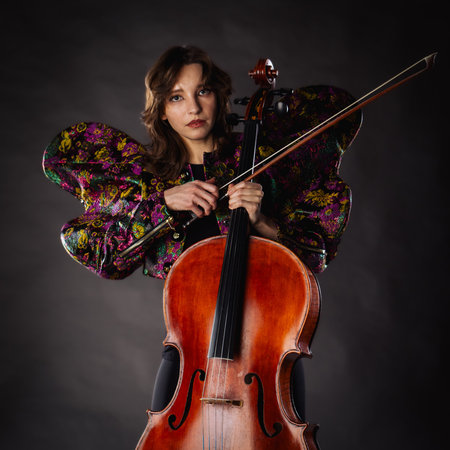 A captivating portrait of cellist Anna Skladannaya against a dark background. She is elegantly...