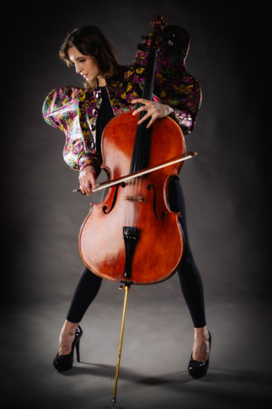 A captivating portrait of a cellist against a dark background. She is elegantly dressed in a floral...