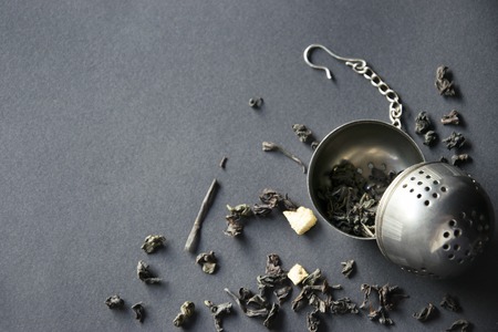 Tea strainer with scattered green tea on dark background, Top viewの写真素材