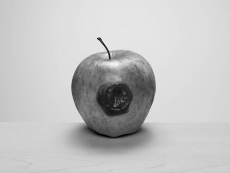 Bruised apple starting to rot on wood table. Black and white. Concept: rotten to the core, one bad apple...の写真素材