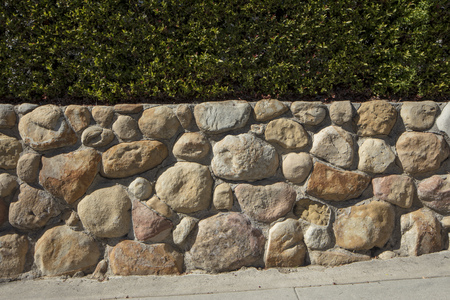 Horizontal detail view of a sandstone wall with a green hedge aboveの写真素材