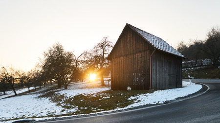 wooden cabin in sunset, winter with dark street in the front of view, snowの写真素材