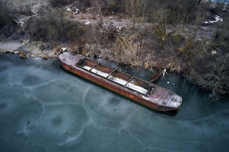 Old boat ship, trapped, frozen in winter ice lake, docked in pier, aerial top down view