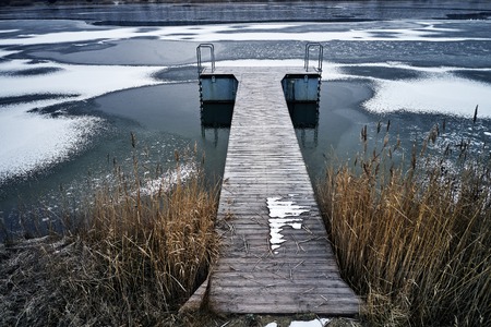 wooden pier on frozen lake on winter, snow and brown grassの写真素材