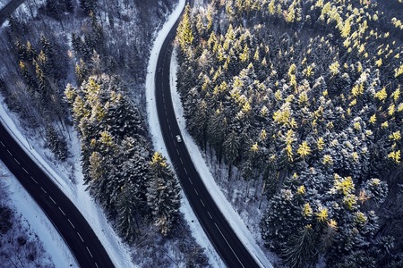 Aerial drone view of a curved winding road through the forest high up in the mountains in the winter with snow covered trees and curved streets in winterの写真素材
