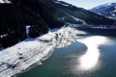 panoramic view of a reservoir lake at winter with cracked mud around. Water in the high alps in austria by day with beautiful light.の写真素材