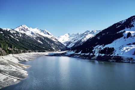 panoramic view of a reservoir lake at winter with cracked mud around. Water in the high alps in austria by day with beautiful light.の写真素材