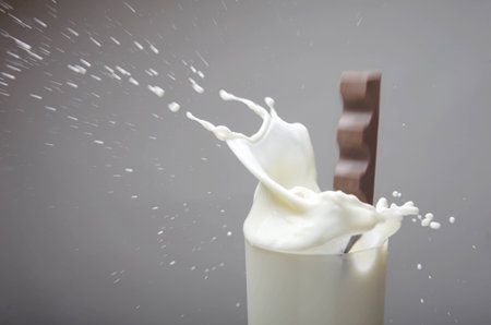 The image shows a chocolate bar splashing in a glass of milkの写真素材