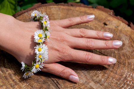 Female hand with daisy flower bracelet in the sun with a wooden surfaceの写真素材