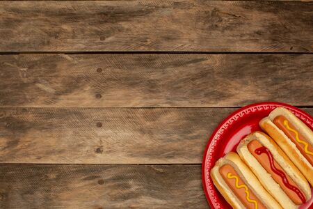 three hot dogs on a red plate and wooden tableの写真素材