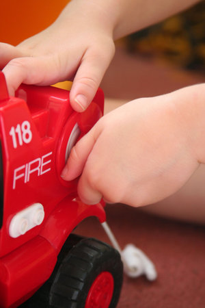 child playing with toy fire truck, turning a knob to retract toy hose