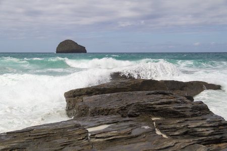 Waves crashing over rocks with Gull rock in the distance at Trebarwith Strandの写真素材