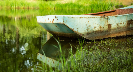 Old boat on the shore of a lake with green grass and reflectionの写真素材