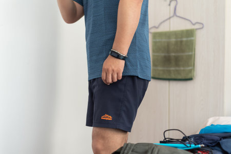 Young man in blue sportswear putting on his shorts while standing at home