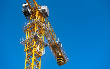 Yellow construction tower crane on blue sky background. Industrial construction machinery.