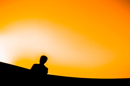 Silhouette of a man sitting on the edge of a cliff at sunset