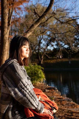 Young asian woman sitting on a rock by the lake in autumnのeditorial素材