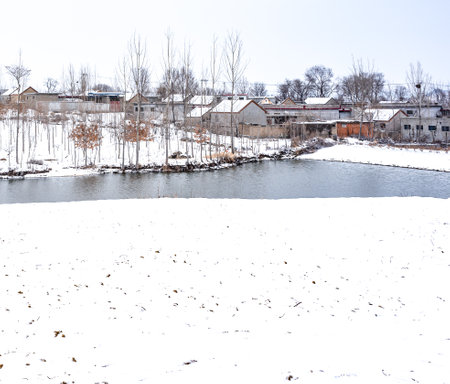 Winter landscape with a small river and snow-covered houses in the backgroundの写真素材