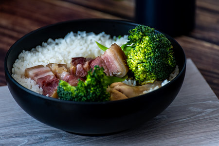 Rice with pork and broccoli in a black bowl on wooden tableの写真素材