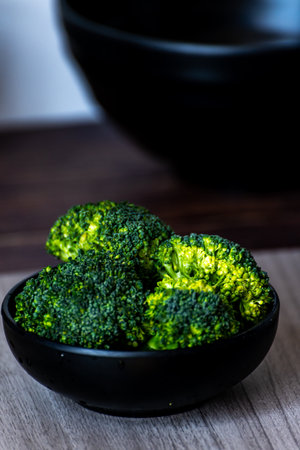 Fresh green broccoli in a black bowl on a wooden table, selective focusの写真素材
