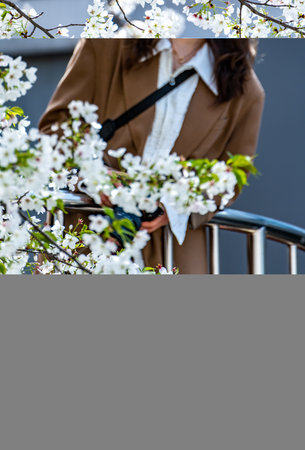 Cropped image of young woman in trench coat standing near blooming tree