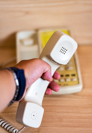 Close-up image of a hand holding a telephone receiver on a wooden background