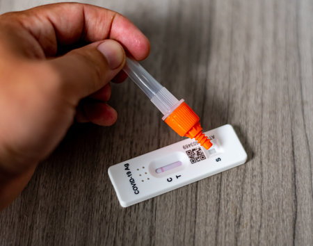 Hand holding a rapid antigen test kit on a wooden table background.の写真素材