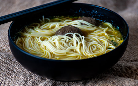 Chinese noodle soup with meatballs in black bowl on jute backgroundの写真素材