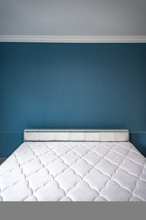 Double bed in a modern bedroom with blue walls and a white mattressの写真素材