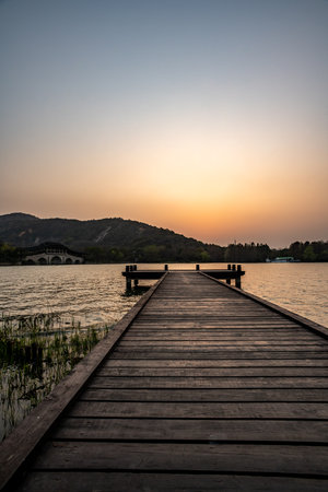 Wooden pier on the lake at sunset with mountains in the backgroundの写真素材