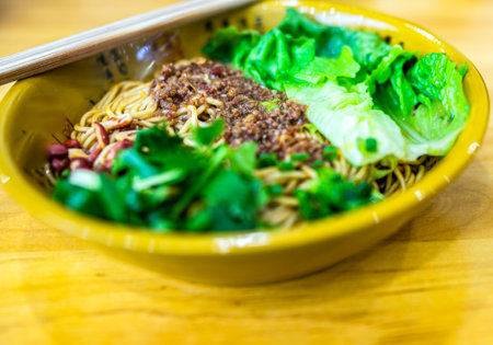 Noodles with minced pork and vegetable in yellow bowl on wooden tableの写真素材