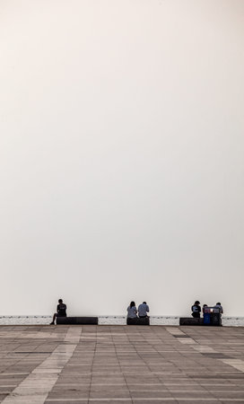 People sitting on the bench and looking at the white wall background.