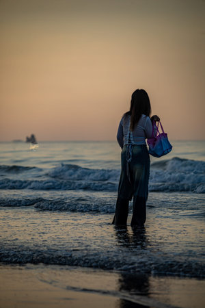 Young woman standing on the beach and looking at the sea at sunset