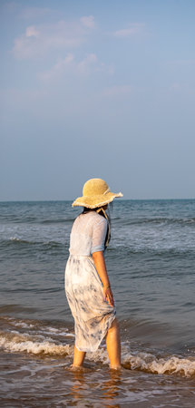A woman in a straw hat walks along the seashore.の写真素材